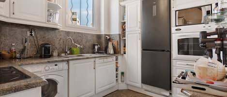 A kitchen with white cabinets, a stainless steel refrigerator, a built-in oven, and a washing machine.