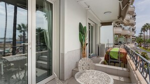 Un balcon avec une table et des chaises, un pot de fleurs et une vue sur la rue et les palmiers.