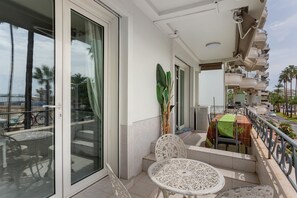 Ein Balkon mit Tisch und Stühlen, einer Topfpflanze und Blick auf die Straße und Palmen.