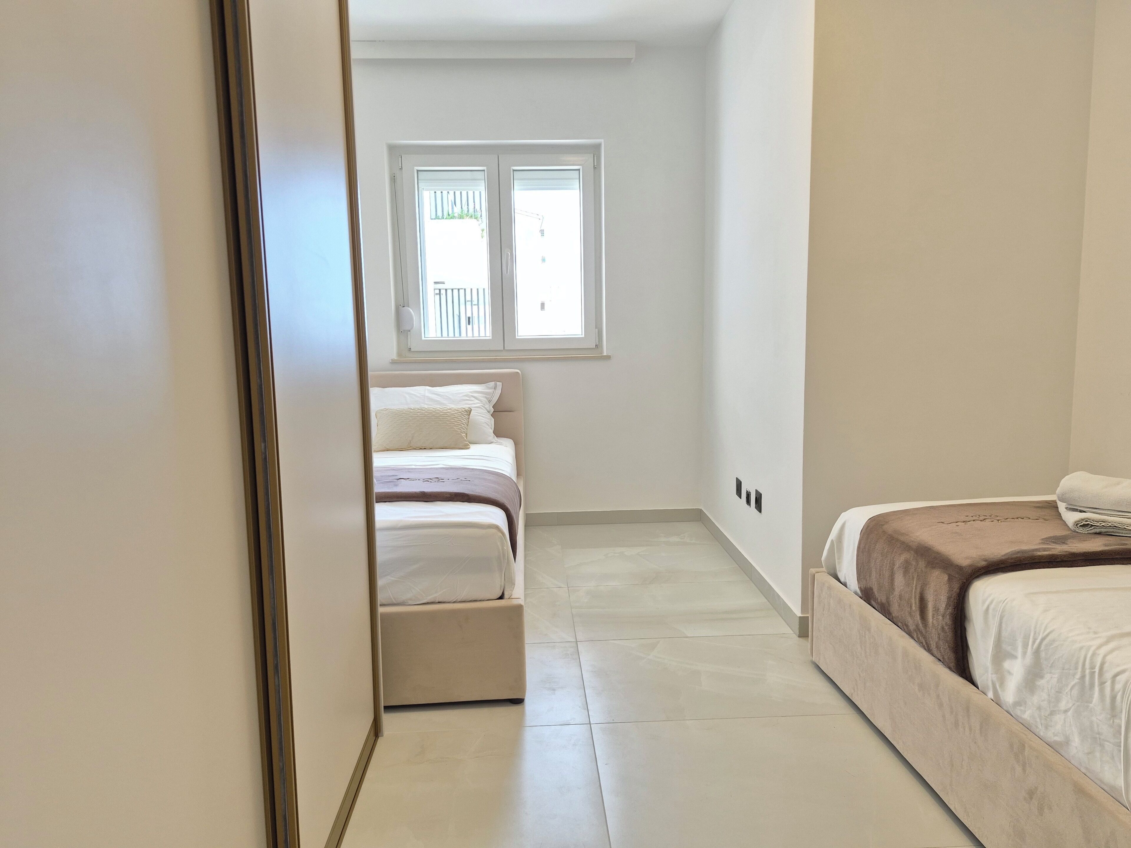 Un couloir étroit mène à une chambre à coucher qui contient un lit, une fenêtre et une porte.