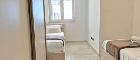 Un couloir étroit mène à une chambre à coucher qui contient un lit, une fenêtre et une porte.