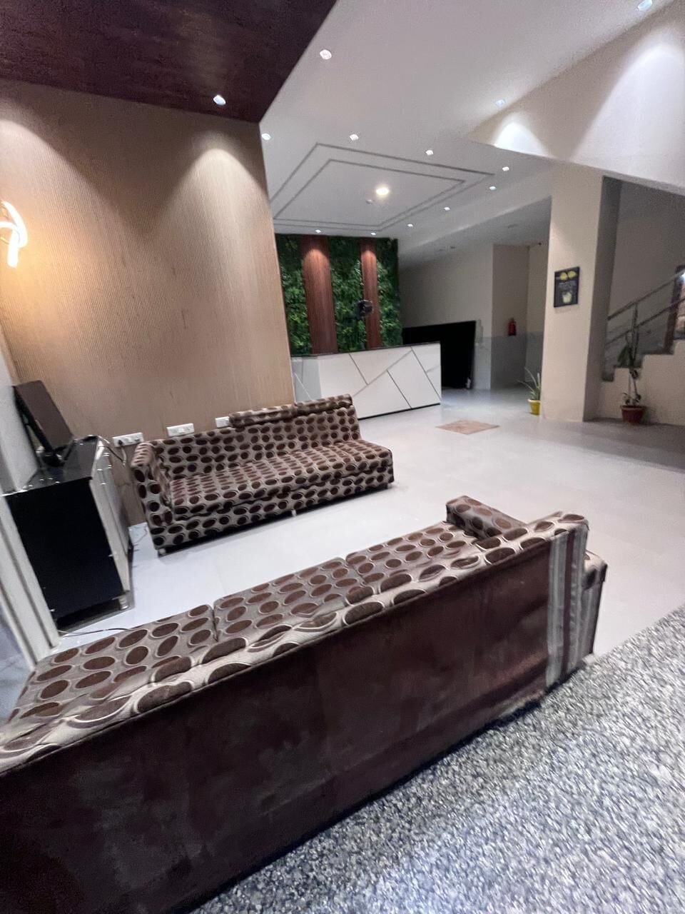 Un vestíbulo moderno con un sofá modular, una mesa de recepción y una escalera.