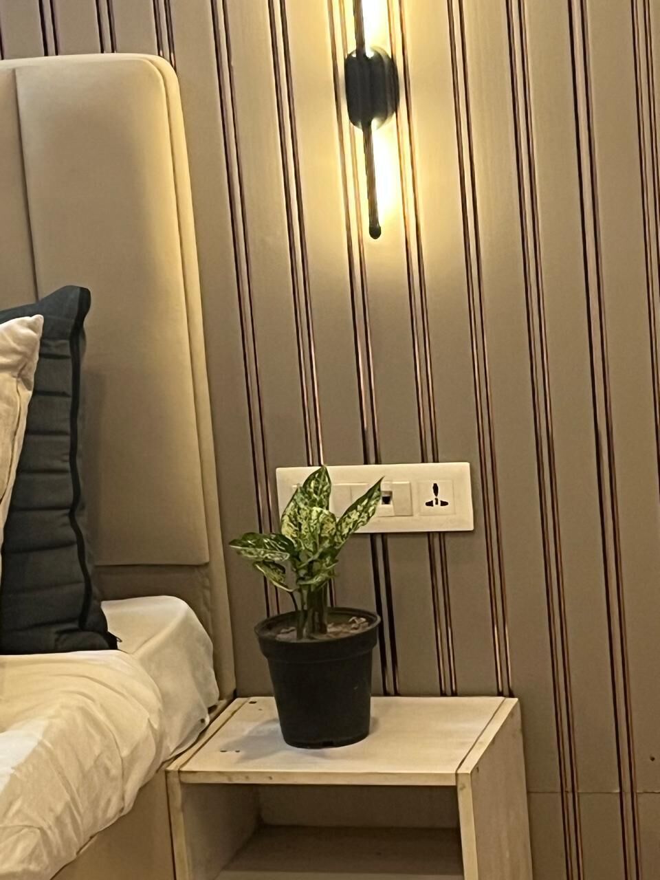 Ein Bett mit Kopfteil, ein Nachttisch mit Blumentopf und eine Wandleuchte.