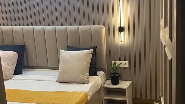 Un dormitorio moderno con cama, mesitas de noche, una planta en maceta y un aplique de pared.