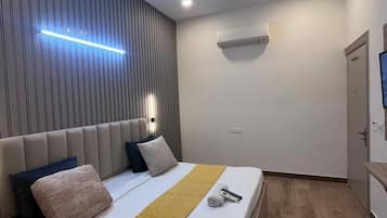 A modern bedroom with a bed, a ceiling fan, recessed lighting, an air conditioning unit, and a wooden floor.