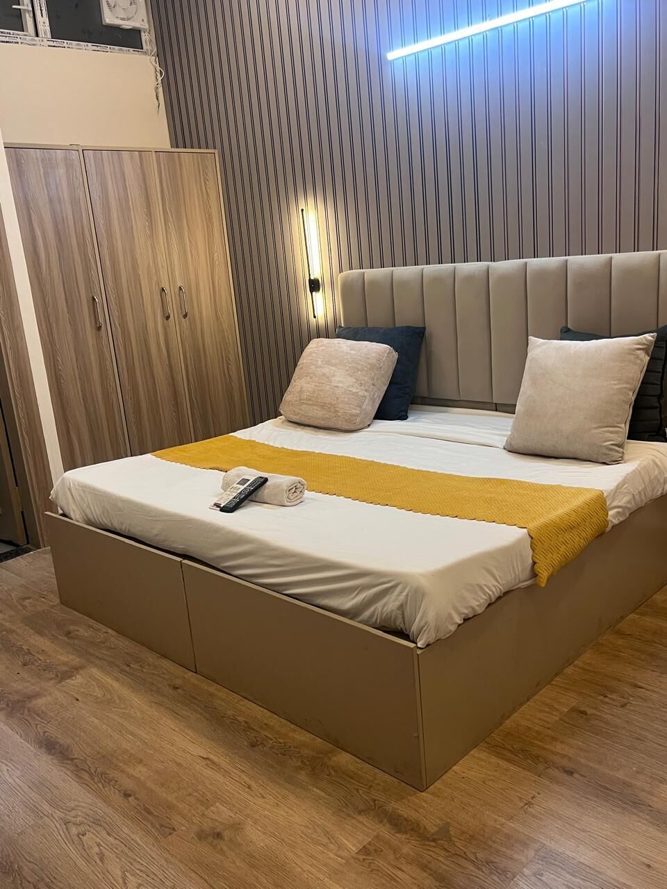 A modern bedroom with a large bed, a wooden wardrobe, and a unique wall panel design.