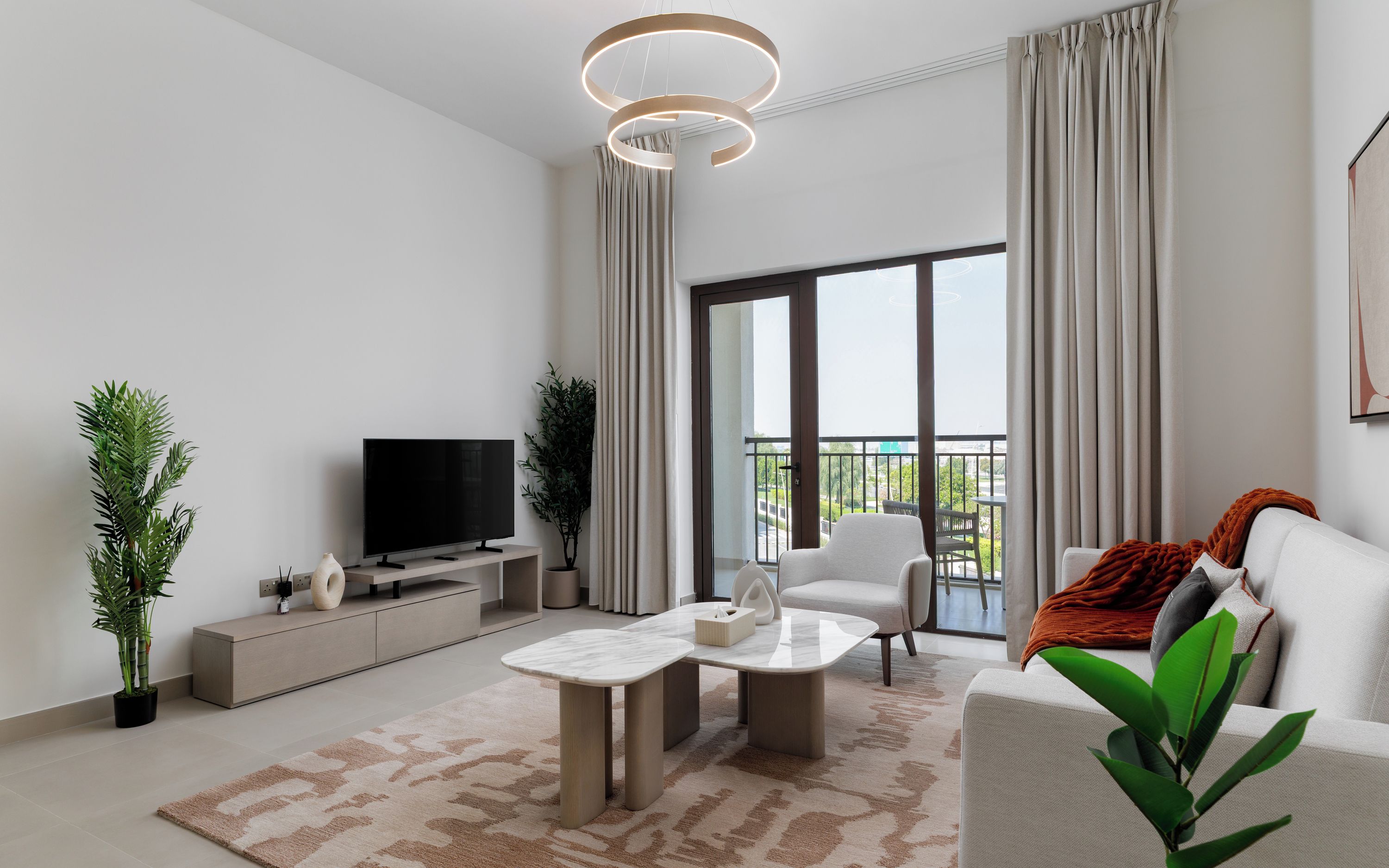 Ein modernes Wohnzimmer mit einem Flachbildfernseher, einem Sofa, einem Couchtisch und einem Balkon mit Vorhängen.