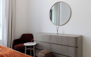 A hotel room with a bed, a red chair, a small round table, a grey console, and a round mirror on the wall. - Maison Privee - Serene Yas Island Hideaway w/ Resort Facilities (Abu Dhabi)