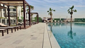A poolside area with lounge chairs and umbrellas, a clear pool, and palm trees. - Maison Privee - Serene Yas Island Hideaway w/ Resort Facilities (Abu Dhabi)