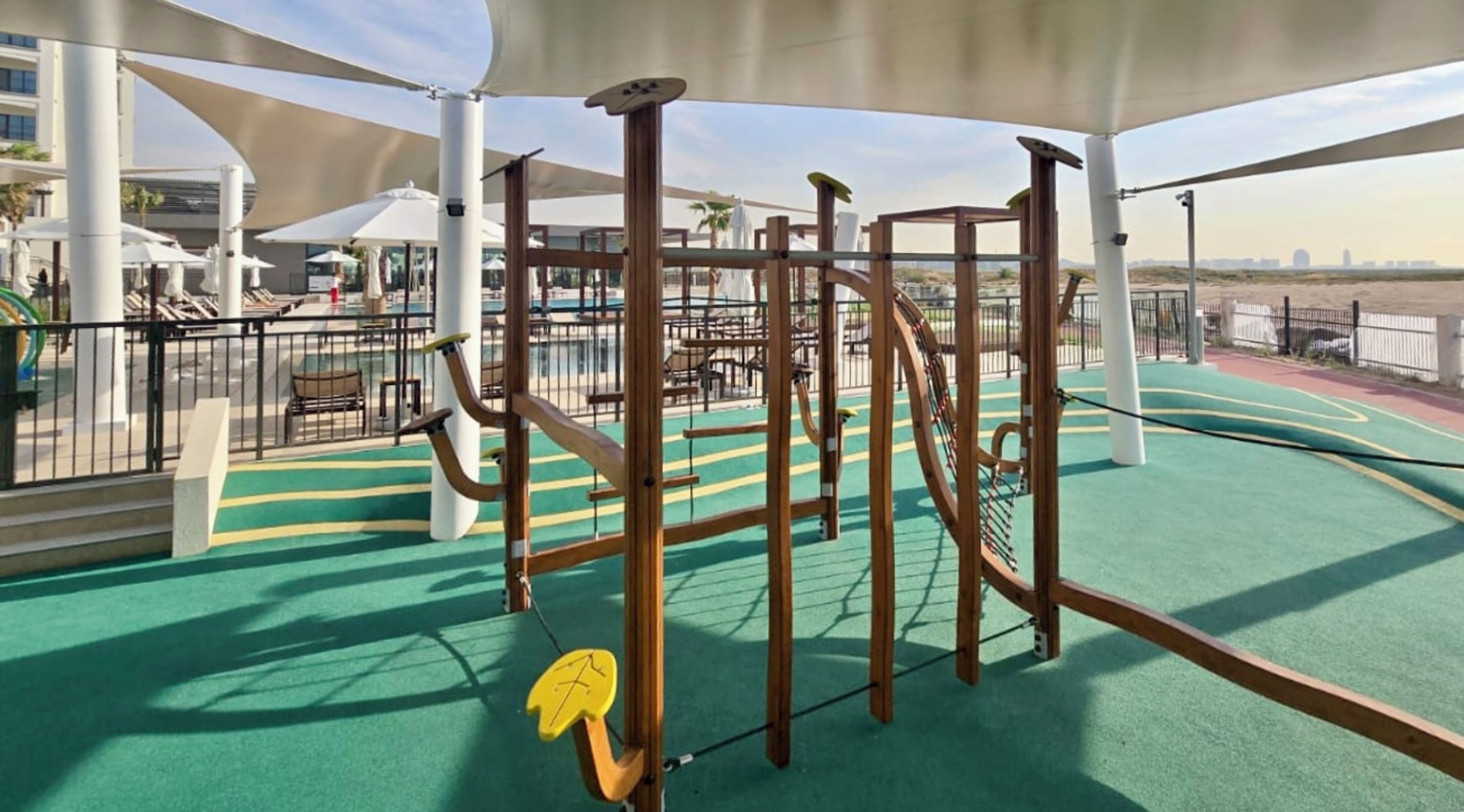An outdoor play area with a climbing structure, exercise equipment, and a green exercise mat.