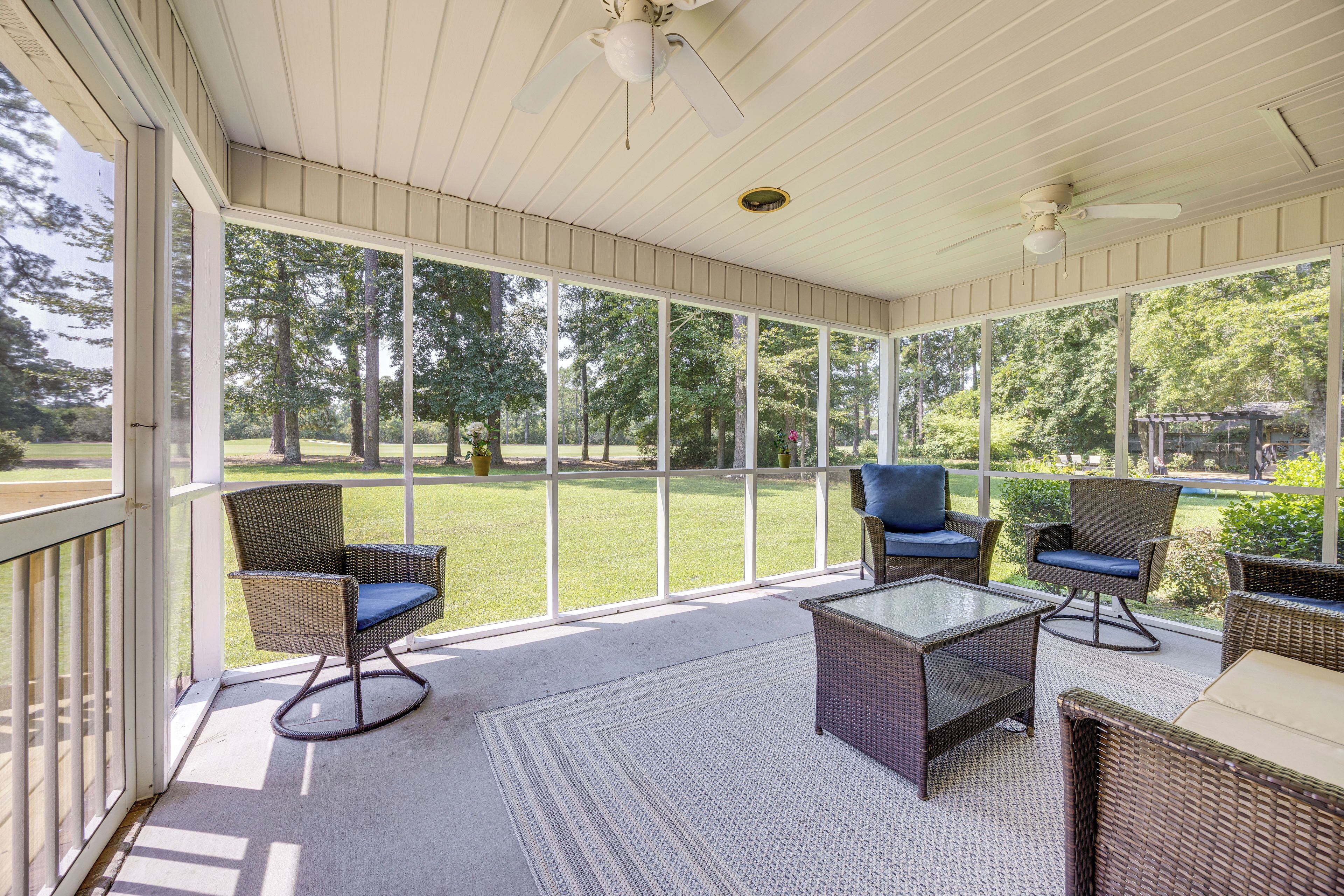 A covered patio area with wicker furniture and a glass table, overlooking a grassy yard.