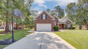 A residential house with a garage, a basketball hoop, and a well-maintained lawn. - Coastal Home on Hackler Golf Course Near CCU (Conway)