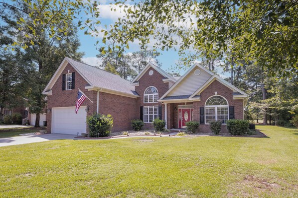 A two-story brick house with a red front door, a garage, and an American flag. - Coastal Home on Hackler Golf Course Near CCU (Conway)