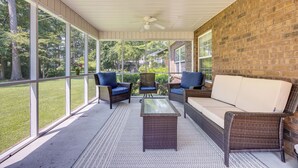 A covered patio with wicker furniture, a glass coffee table, and a brick wall. - Coastal Home on Hackler Golf Course Near CCU (Conway)