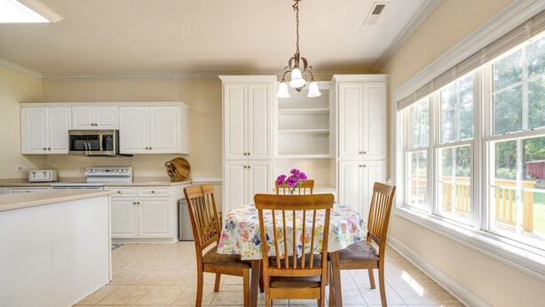 A kitchen with white cabinets, a microwave, a toaster, and a dining table with chairs. - Coastal Home on Hackler Golf Course Near CCU (Conway)