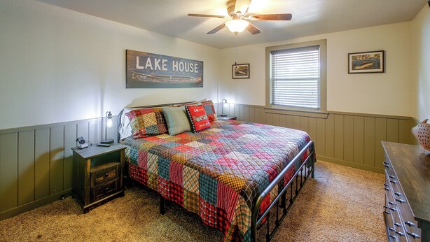 A bedroom with a bed, a nightstand, a ceiling fan, a window with blinds, and a wall with a framed picture and a sign. - Steps to Lake! Cabin w/ Water Views in Hot Springs (Hot Springs)