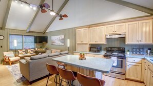 A spacious kitchen with a central island, bar stools, a dining area with a sofa, and a large window with blinds. - Steps to Lake! Cabin w/ Water Views in Hot Springs (Hot Springs)