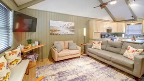 A living room with a beige sofa, a television mounted on the wall, and a painting of birds. - Steps to Lake! Cabin w/ Water Views in Hot Springs (Hot Springs)