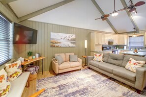 Ein Wohnzimmer mit einem beigen Sofa, einem an der Wand montierten Fernseher und einem Gemälde von Vögeln.