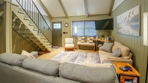 A living room with a staircase, a sofa, a coffee table, and a television. - Steps to Lake! Cabin w/ Water Views in Hot Springs (Hot Springs)