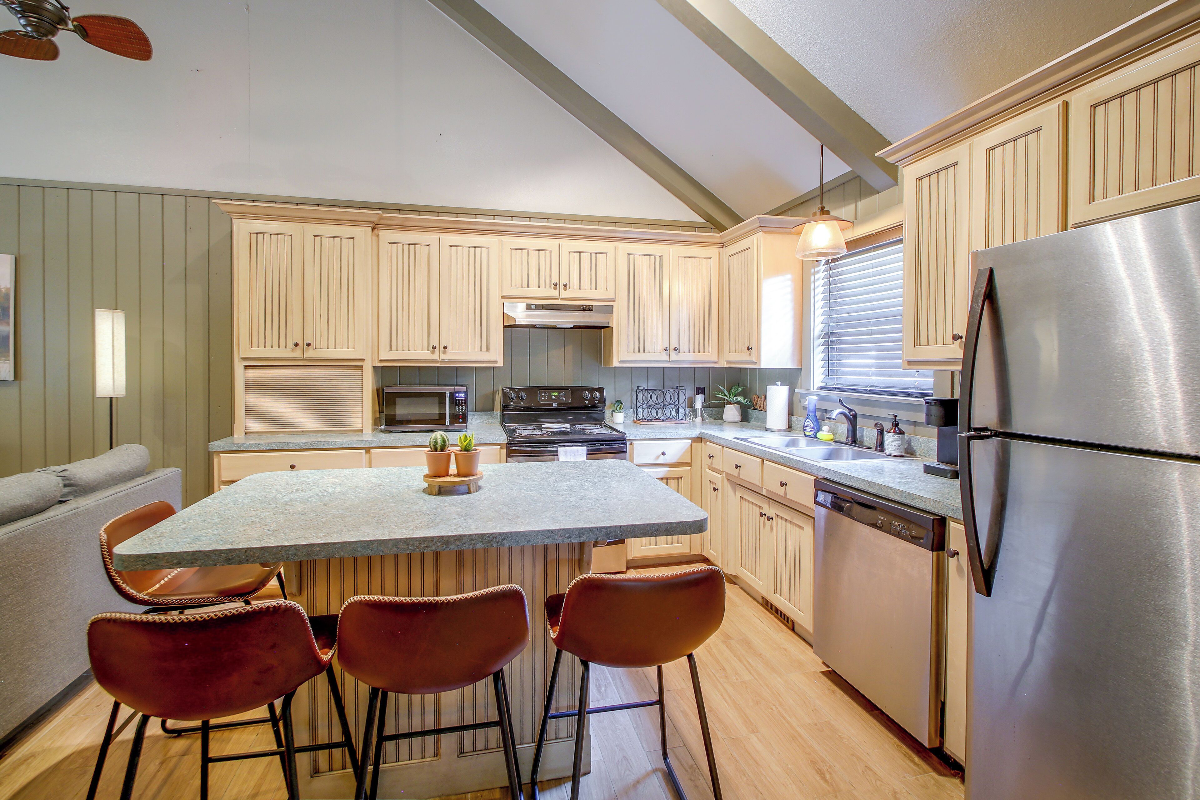 A kitchen with a central island, bar stools, a refrigerator, and wooden cabinets.