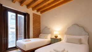 A hotel room with two beds, a balcony, wooden ceiling beams, and a brick wall. - Isabel de Castilla - Apartamento Premium (Avila)