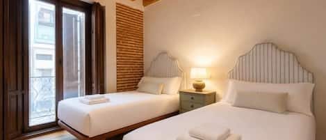 A hotel room with two beds, a balcony, wooden ceiling beams, and a brick wall.