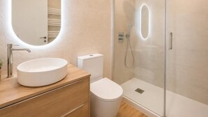 A modern bathroom with a round mirror, a white sink, a toilet, and a glass-enclosed shower. - Isabel de Castilla - Apartamento Premium (Avila)