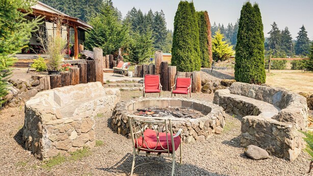 A rustic outdoor seating area with stone walls, a fire pit, and red chairs. - Ranch Suite w/ Hot Tub! Couple’s Stay in La Center (La Center)