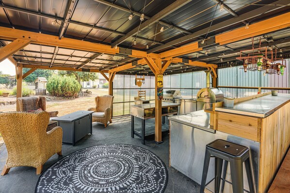 A covered outdoor area with a grill station, seating, and a patterned rug.