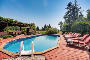 An outdoor swimming pool with a wooden deck, lounge chairs, and a pergola.
