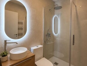 Ein modernes Badezimmer mit rundem Spiegel, Waschbecken, Toilette und Duschkabine.