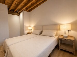 Ein Doppelbett mit zwei Nachttischen, jeweils mit einer Lampe, in einem Zimmer mit Holzbalkendecke.