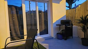 Eine Terrasse mit Glastür, Grill, Stuhl und einer Topfpflanze.