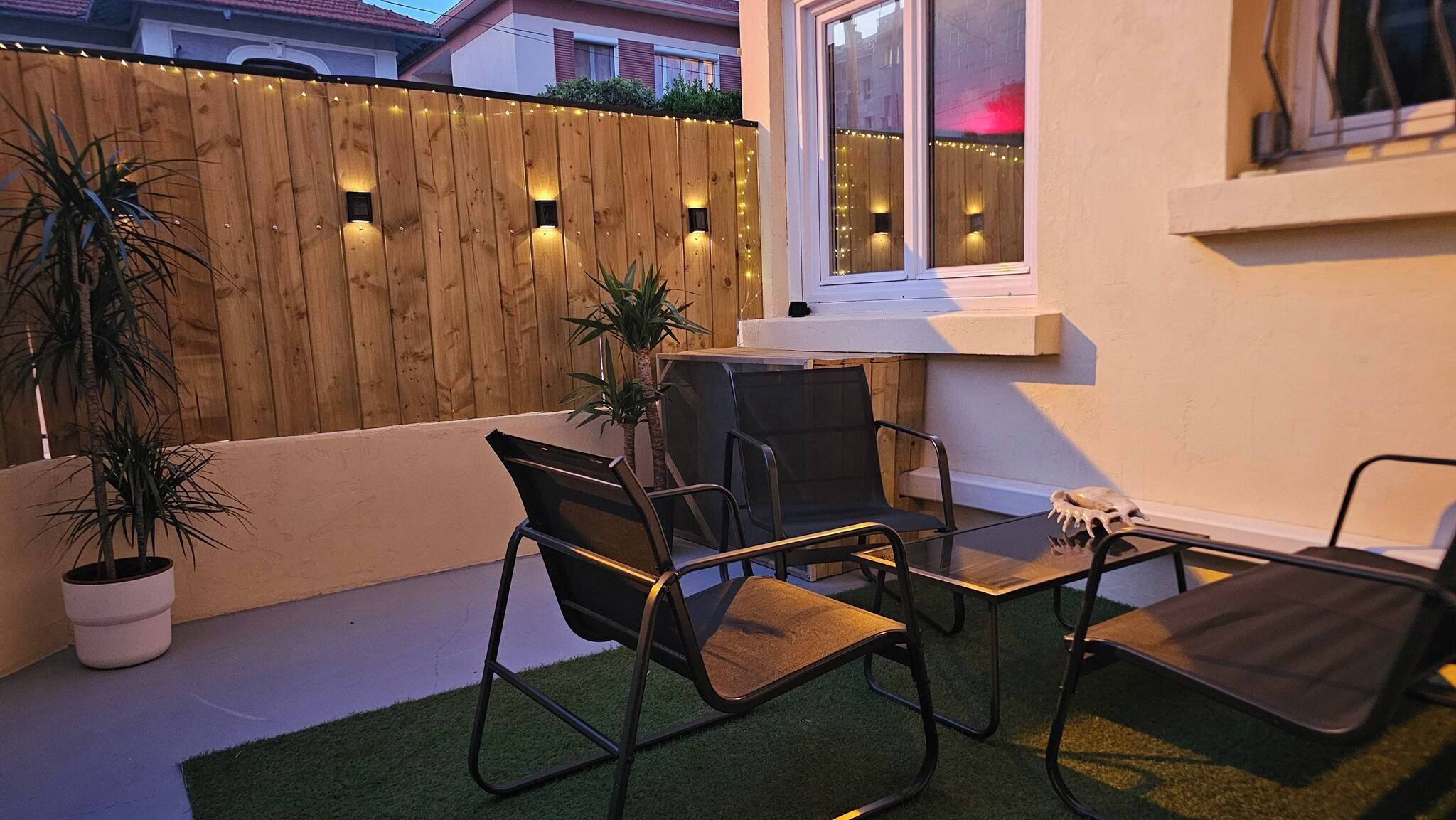 A patio with a wooden fence, two chairs, a small table, and a potted plant.
