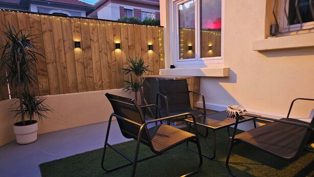 Un patio con cerco de madera, dos sillas, una mesita y una planta en maceta.