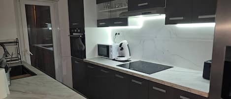 A modern kitchen with dark cabinets, a microwave, a coffee maker, and a built-in stove.