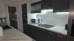 Eine moderne Küche mit dunklen Schränken, einer Mikrowelle, einer Kaffeemaschine und einem eingebauten Herd.
