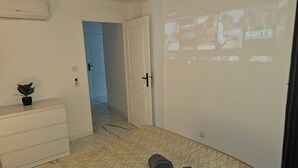 Un dormitorio con cama, cómoda, planta, puerta y una pantalla de proyección mostrando imágenes.