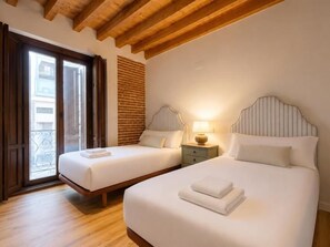 Een hotelkamer met twee bedden, een balkon, houten balken in het plafond en een bakstenen muur.