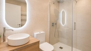 A modern bathroom with a round mirror, a white sink, a toilet, and a glass-enclosed shower. - Juana I de Castilla - Apartamento Premium (Avila)