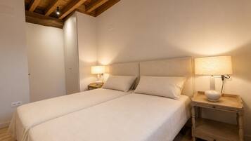 A double bed with two bedside tables, each with a lamp, in a room with wooden beams on the ceiling.