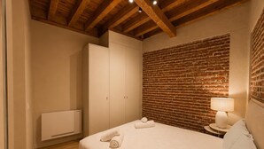 Ein Schlafzimmer mit Backsteinwand, einem Bett mit weißer Bettdecke, einem Nachttisch mit Lampe und einem Kleiderschrank.