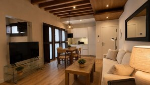 Ein modernes Wohnzimmer mit Holzbalkendecke, einem Glastisch, einer Couch und einem Fernseher.