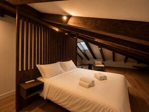 Ein Schlafzimmer mit schrägem Dach, einem Bett mit weißen Leinentüchern, einem Sessel und einem kleinen Tisch.