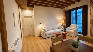 A living room with a white sofa, a wooden dining table, and a brick wall. - Santa Teresa de Jesús - Apartamento Deluxe (Avila)