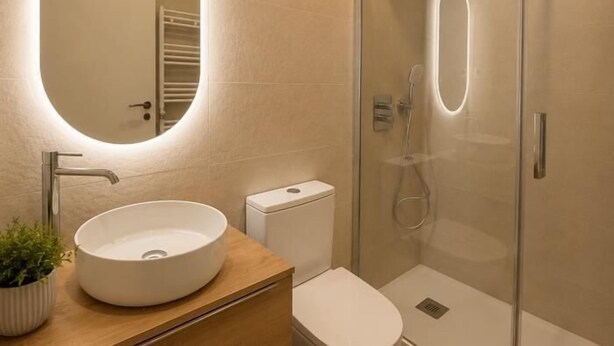 A modern bathroom with a round mirror, a sink, a toilet, and a glass-enclosed shower. - María de Molina - Apartamento Deluxe (Avila)
