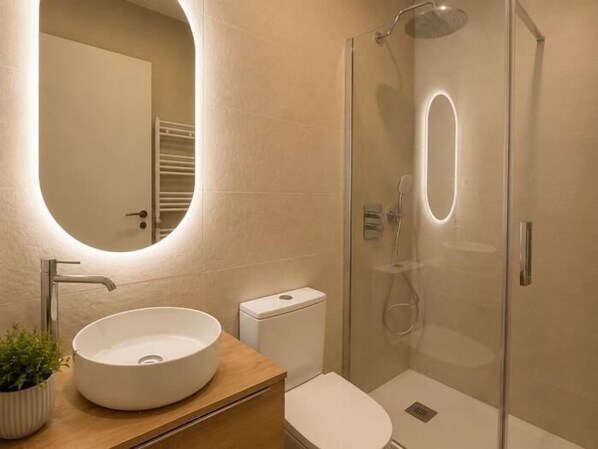 A modern bathroom with a round mirror, a sink, a toilet, and a glass-enclosed shower.