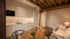 A modern kitchen with white cabinets, a wooden dining table with chairs, and a built-in microwave. - María de Molina - Apartamento Deluxe (Avila)