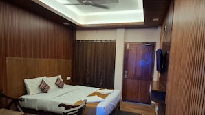 A hotel room with a bed, a desk, a chair, a television, and a door. - My Island Residency (Port Blair)